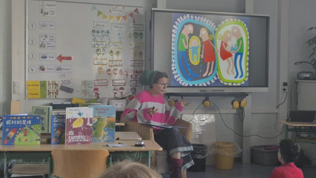 Autorin liest im Klassenraum vor, vor ihr Bücher auf einem Tisch