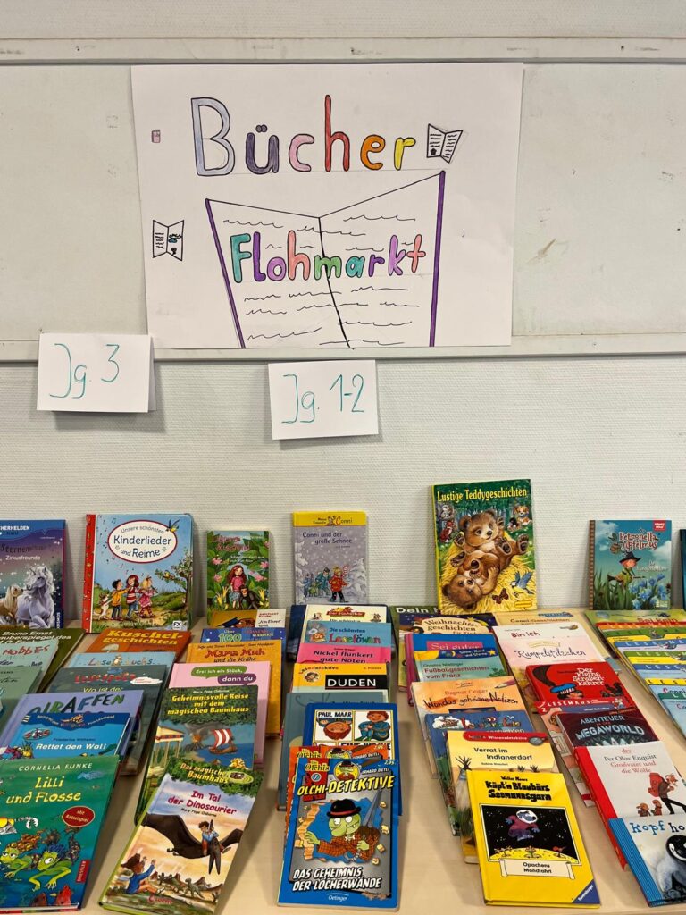 Kinderbücher liegen zum Verkauf auf Tischen, darüber das Bücherflohmarkt-Plakat