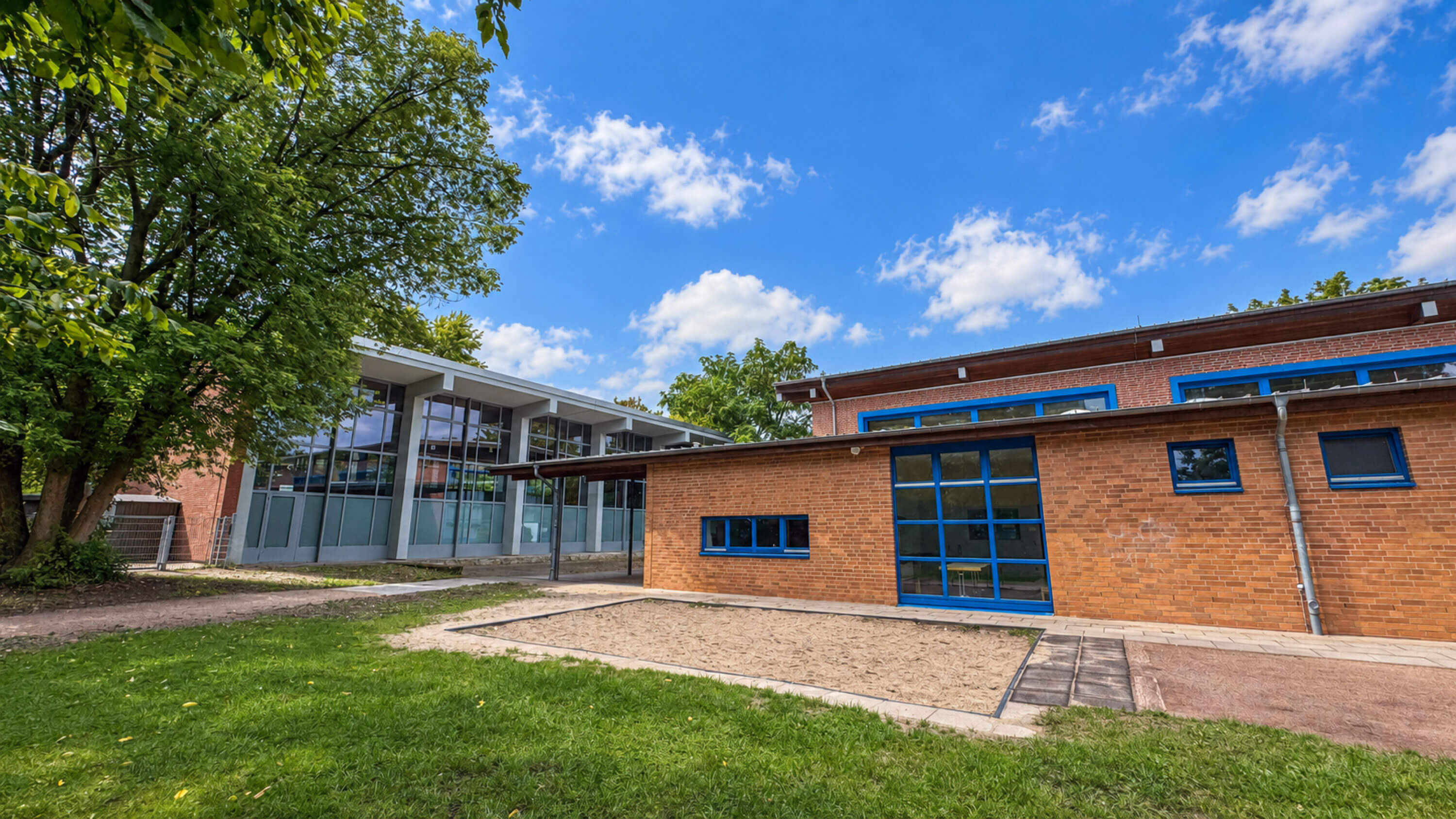Flacher Klinkerbau mit blauen Fensterrahmen und Rasenfläche