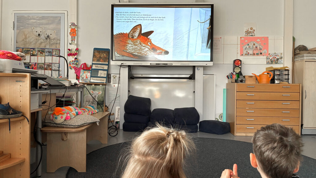 Kinder sitzen vor der digitalen Tafel, auf der ein Fuchs zu sehen ist