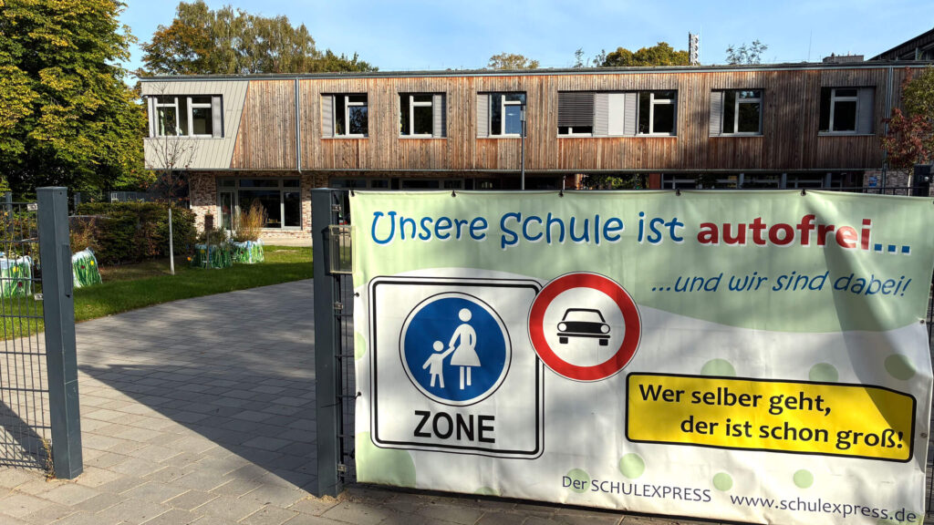 Banner am Schultor: „Unsere Schule ist autofrei“ mit Hinweis auf den Schulexpress