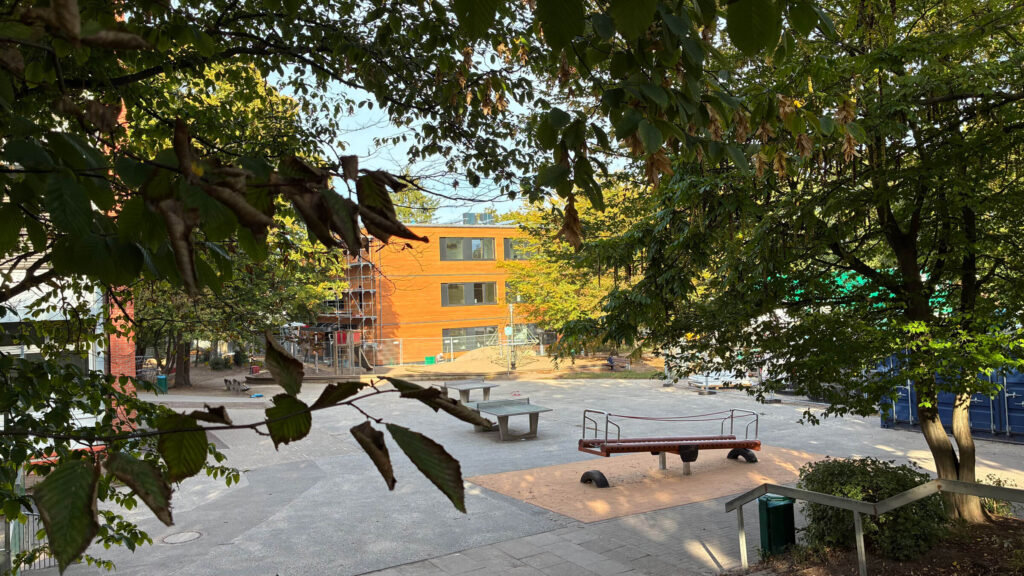 Schulhof unter Bäumen mit Sitzbänken und Spielgerät